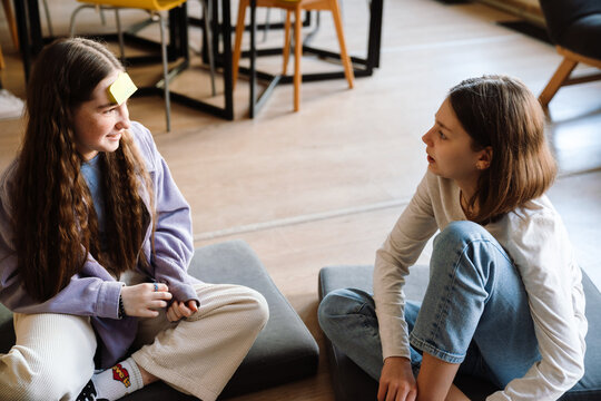 School girl playing guess who game with her friend while sitting in classroom