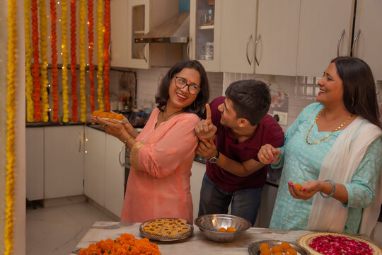 Young boy trying to steal Ladoos ( a Traditional Indian Sweet) as his mother and aunt make them during the festival of Diwali 
