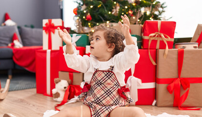 Obraz na płótnie Canvas Adorable hispanic girl sitting on floor by christmas tree at home