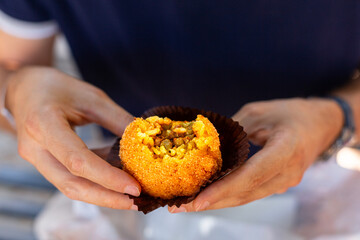 A man eating arancini, italian rice ball al ragu or al sugo, that is stuffed  with meat, peas and tomato sauce and spices, coated with breadcrumbs and deep fried. Sicilian street food, cuisine.