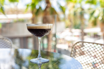 Aperitif with Caffè shakerato in a tall glass, in an outdoor italian cafe, palms on background....