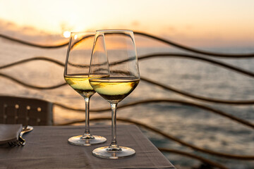 Romantic outdoor evening with two glasses of white wine and beautiful sunset on the sea beach at background. Italy, Sicily, evening time, summer.