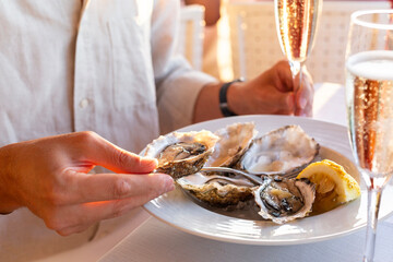 A man Eating Raw Oysters with lemon and ice served and holding a glass of champagne, wine. Seafood...