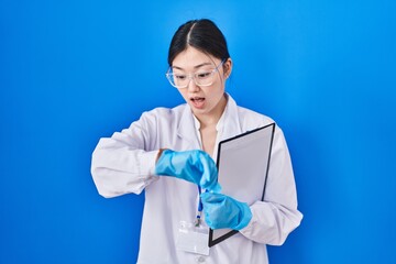 Chinese young woman working at scientist laboratory looking at the watch time worried, afraid of getting late