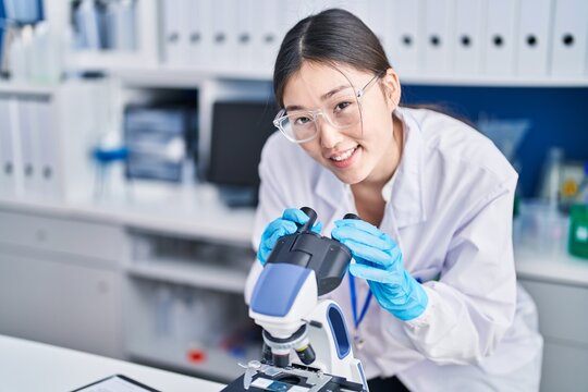 Chinese woman scientist smiling confident using microscope at laboratory
