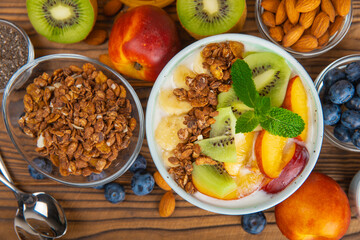 Bowl of granola with yogurt and fresh berries on a texture table. Yogurt berries, acai bowl, spirulina bowl. Healthy food, balanced breakfast. Strawberries, blueberries, kiwi, peach, almonds and chia.