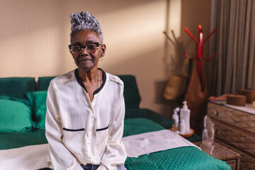 Senior woman with stylish afro hair sitting on bed with serious expression.