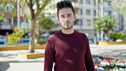 Young hispanic man standing with serious expression at park