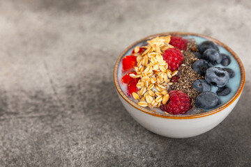 Bowl of granola with yogurt and fresh berries on a texture table. Yogurt berries, acai bowl, spirulina bowl. Healthy food, balanced breakfast. Strawberries, blueberries, kiwi, peach, almonds and chia.