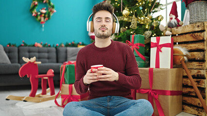 Young hispanic man listening to music drinking coffee celebrating christmas at home