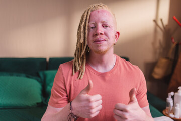Homem albino sentado na cama dando sinal de positivo.