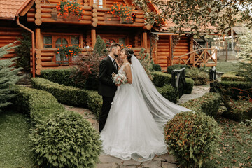 gorgeous elegant luxurious bride with veil blowing in the wind. and a stylish groom kiss outdoors near tall autumn trees