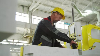 Low angle shot of mature male worker in hardhat and uniform measuring marble slab with tape during workday at stone factory