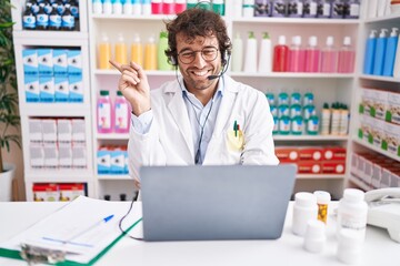 Hispanic young man working at pharmacy drugstore working with laptop smiling happy pointing with...