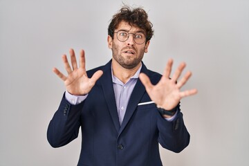 Hispanic business man wearing glasses afraid and terrified with fear expression stop gesture with hands, shouting in shock. panic concept.