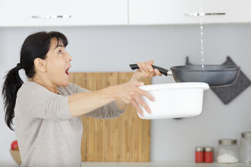 mature woman holding bucket while water droplets leak from ceiling