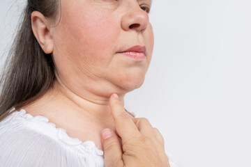 Obraz premium Woman 50 years old touching hand to fat double chin, examines wrinkles on skin, facelift, age-related skin changes, aesthetic injection cosmetology, care anti-aging procedures