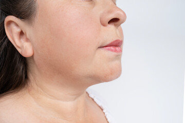 close-up face, adult middle-aged woman 45 years old looking at age-related wrinkles on neck and...