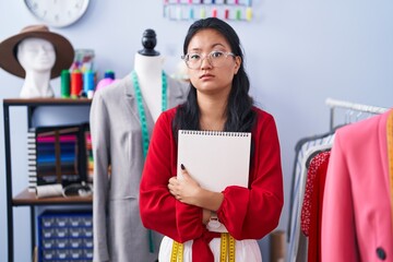 Asian young woman dressmaker standing by manikin skeptic and nervous, frowning upset because of problem. negative person.