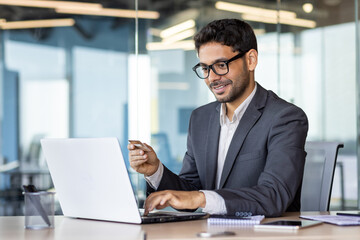 Happy successful businessman with bank credit card inside office at workplace, man using laptop for online shopping and money transfer.