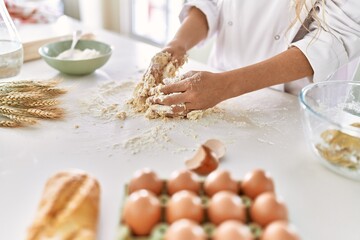 Young woman wearing cook uniform kneading flour at kitchen