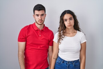 Young hispanic couple standing over isolated background depressed and worry for distress, crying...