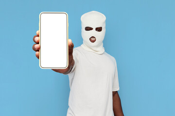 african american man thug in white balaclava shows empty smartphone screen on blue isolated...