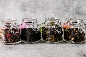 Assortment of glass jars filled with dry tea on defocused background.