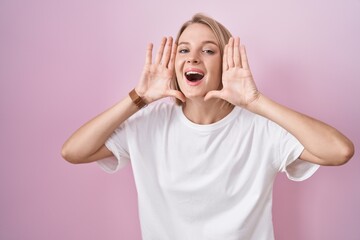 Young caucasian woman standing over pink background smiling cheerful playing peek a boo with hands...