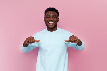 african american man in blue sweater points with his hands at himself on pink isolated background