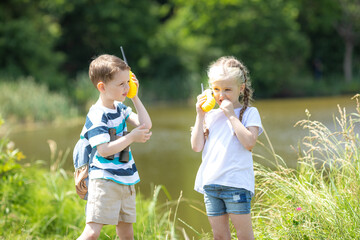 Two children boy and girl 5-6 years old with a backpack talking on a walkie-talkie in the forest,...
