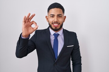 Young hispanic man wearing business suit and tie smiling positive doing ok sign with hand and fingers. successful expression.