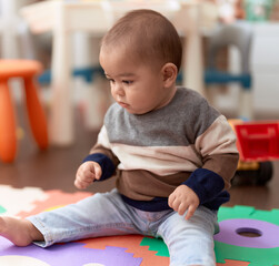 Adorable chinese toddler sitting on floor with serious expression at kindergarten
