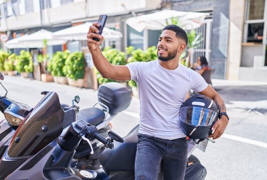 Young latin man make selfie by smartphone standing by motorbike at street