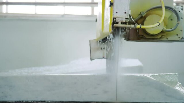 Medium shot of water running over while marble block from top of industrial machine at natural stone factory