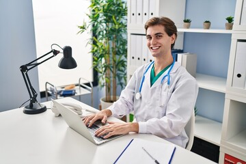 Young caucasian man doctor smiling confident using laptop working at clinic