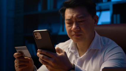 Puzzled confused Asian man failure pay Korean businessman bank credit card online payment problem financial trouble blocked money unsuccessful transaction mobile phone error at night evening office