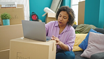 Young beautiful latin woman using laptop sitting on sofa at new home