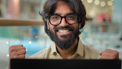 Happy excited Indian worker man in glasses celebrate business success online winning good result...
