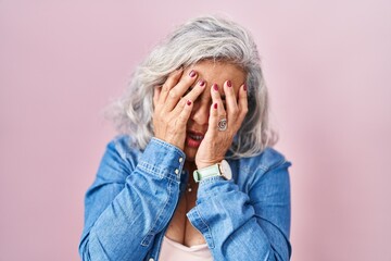 Middle age woman with grey hair standing over pink background rubbing eyes for fatigue and...