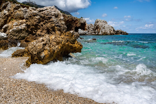 A secluded bay with shiny gravel and turquoise waters in the Mediterranean Sea between the rocks of the Zingaro National Park in Sicily in the sun