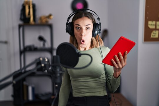 Hispanic woman singing song using microphone and tablet scared and amazed with open mouth for surprise, disbelief face
