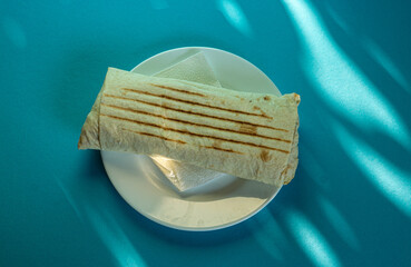 Large shawarma on a white plate with a napkin on a blue background with shadows. Food, healthy fast food, delicious to eat.