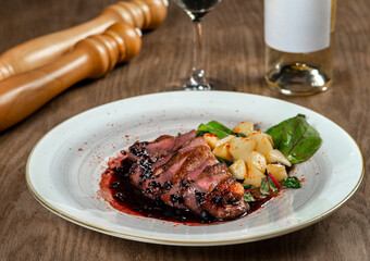 Sliced duck breast with potatoes and wine on wooden table