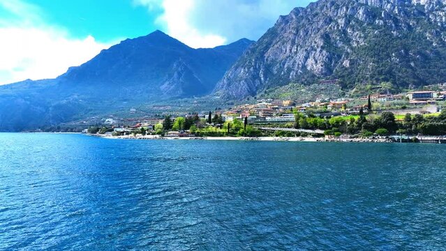 Aerial Shot Of Blue Lake Garda Near Town And Mountain Ranges, Drone Flying Forward Towards Beach Against Sky - Limone sul Garda, Italy