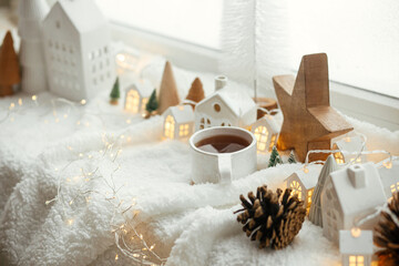 Stylish cup of tea with modern christmas houses, pine cone, wooden star and tree decor, golden...