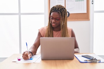 African american woman business worker using laptop writing on document at office