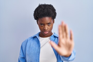 African american woman standing over blue background doing stop sing with palm of the hand. warning...