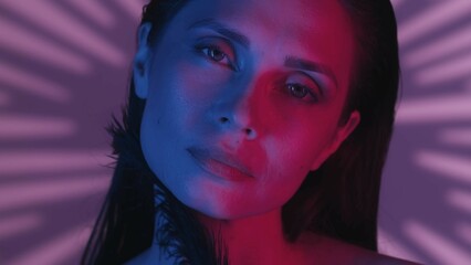 Close up shot of a young woman's face turned at the camera with a relaxed look in a neon pink and blue light.