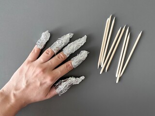The process of removing gel polish from nails. Nails wrapped in foil on a gray background.